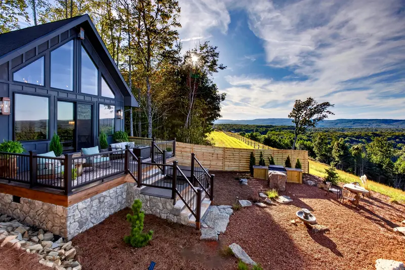 The A-frame, stone-clad deck and landscaped grounds in afternoon light