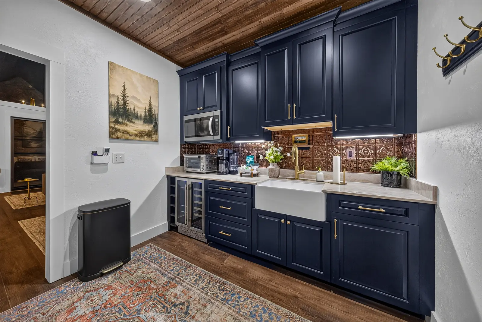 The kitchenette with navy cabinetry, a farmhouse sink, copper backsplash and a wine refrigerator