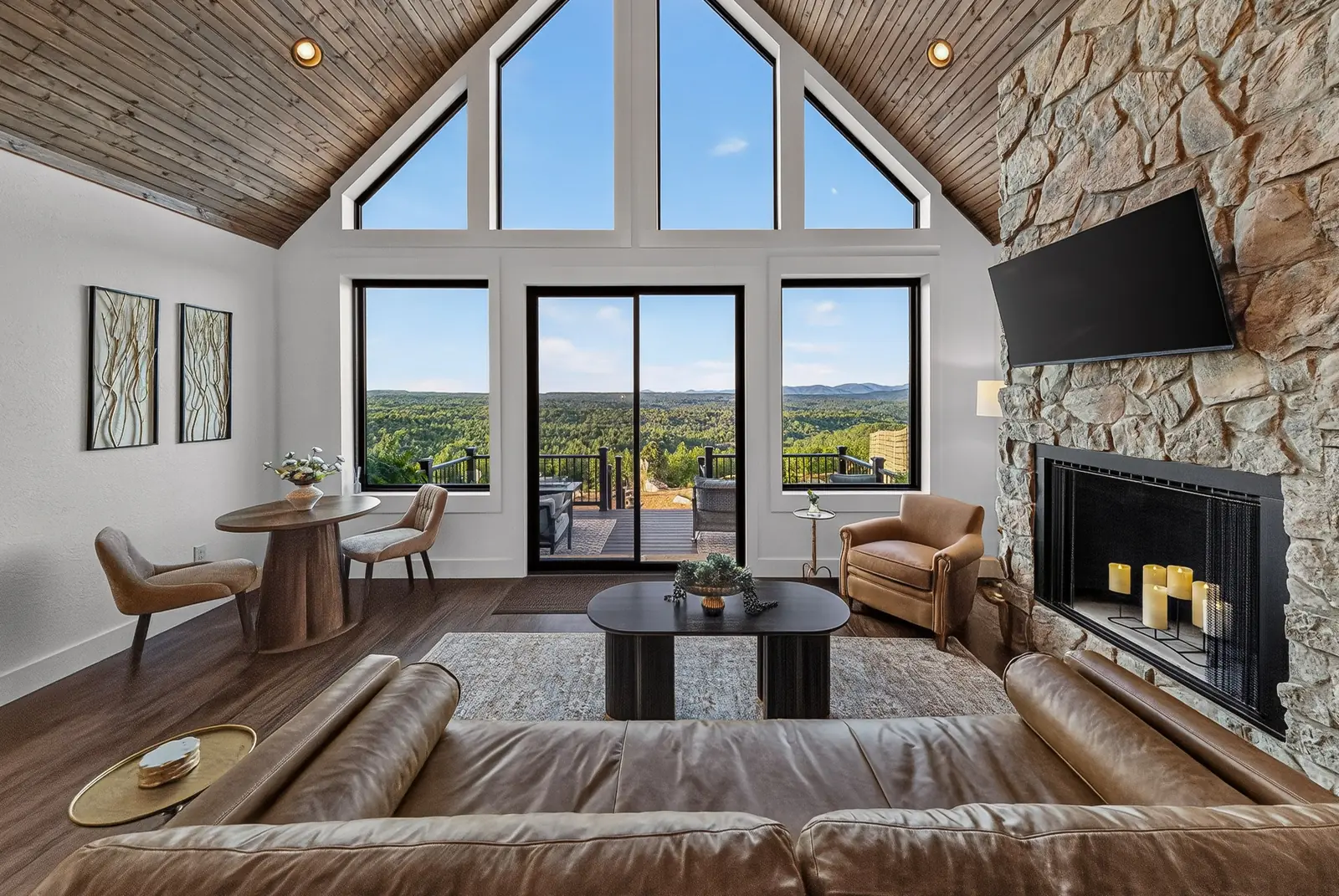 The great room with a vaulted wood ceiling, stone fireplace, leather sofa and floor-to-ceiling windows framing the mountains