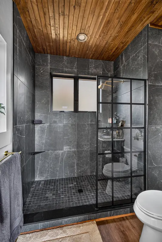 The walk-in shower in dark stone tile with black-framed glass